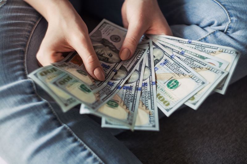 woman holding fanned out 100 dollar bills